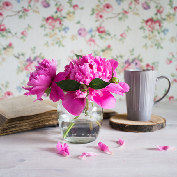 ramo fresco de peonías en un frasco de vidrio sobre una mesa de madera blanca. libro y una taza de té
 - Foto, Imagen