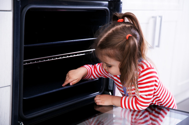 Little girl playing with oven in the kitchen - 写真・画像