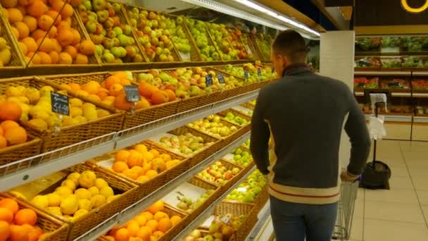 買い物カゴを持つ男は、大型スーパー マーケットでオレンジを選択します。 - 映像、動画