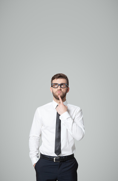 Young handsome businessman thinking on gray background. - Photo, image