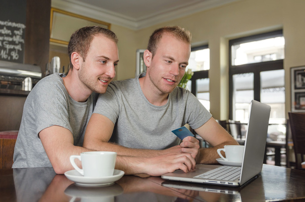 χαμογελώντας γκέι ζευγάρι κάνει online τραπεζικές συναλλαγές στον φορητό υπολογιστή τους - Φωτογραφία, εικόνα