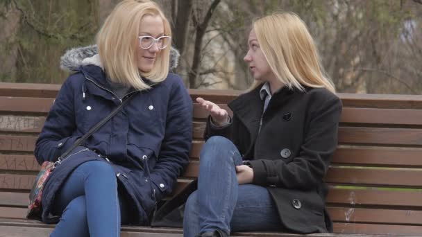 Dos chicas sentadas en el banco en el parque de la ciudad y hablando
 - Imágenes, Vídeo