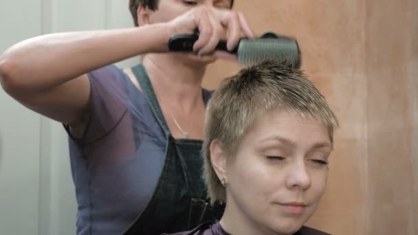 Friseur trocknet und stylt kurze Haare blonden Kopf - Filmmaterial, Video