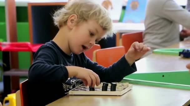 男の子は、幼稚園でチェッカーを再生します。ゲームについての情熱が、笑う、喜ぶ.  - 映像、動画