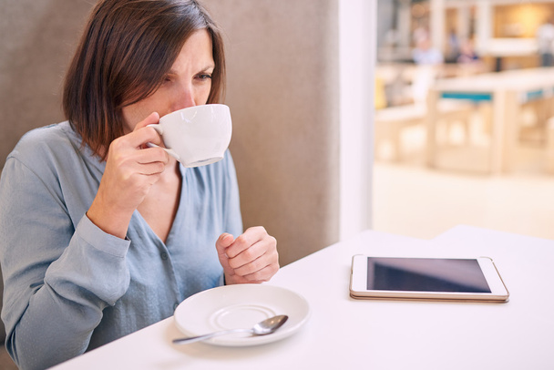 woman sipping cappaccino in a bright cafe with tablet - Foto, afbeelding