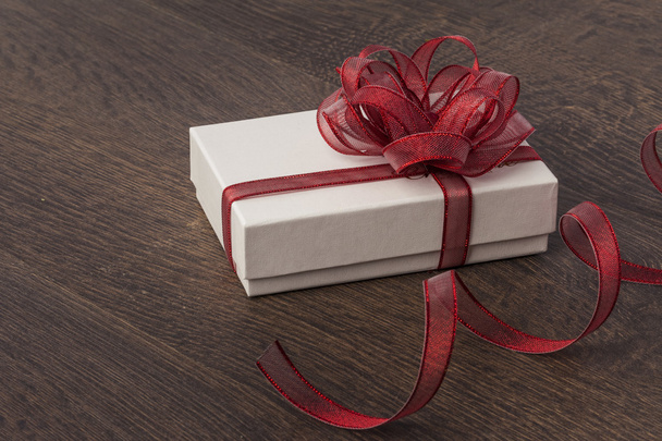 Подарочная коробка с красным бантом на фоне дерева
 - Фото, изображение