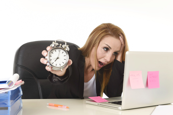 attractive blond businesswoman holding alarm clock overwhelmed in stress working with computer - Photo, Image