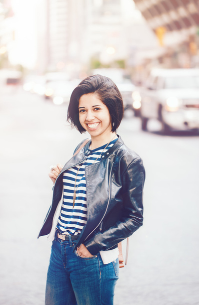 Портрет красивой улыбающейся молодой кавказской латиноамериканки с темно-коричневыми глазами и короткими темными волосами в синих джинсах, кожаная куртка байкера на городской улице, тонизированная фильтрами Instagram
 - Фото, изображение