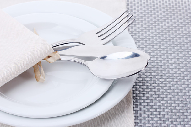 White empty plates with fork, spoon and knife tied with a ribbon on a grey tablecloth - Fotó, kép