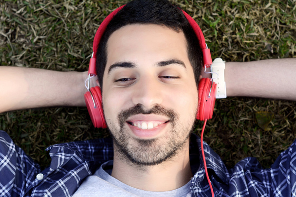 Young man listening to music with headphones in park. - Zdjęcie, obraz