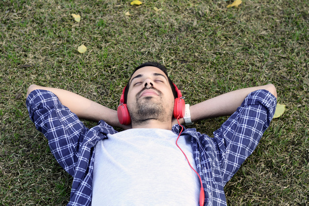 Young man listening to music with headphones in park. - Fotó, kép