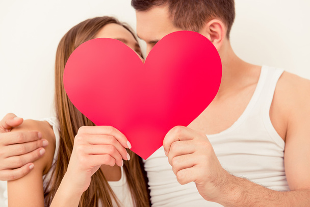 Close up portrait of man and woman kissing behind paper heart - Фото, изображение