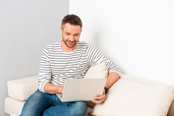 Handsome man sitting on sofa and reading news on laptop - Fotoğraf, Görsel