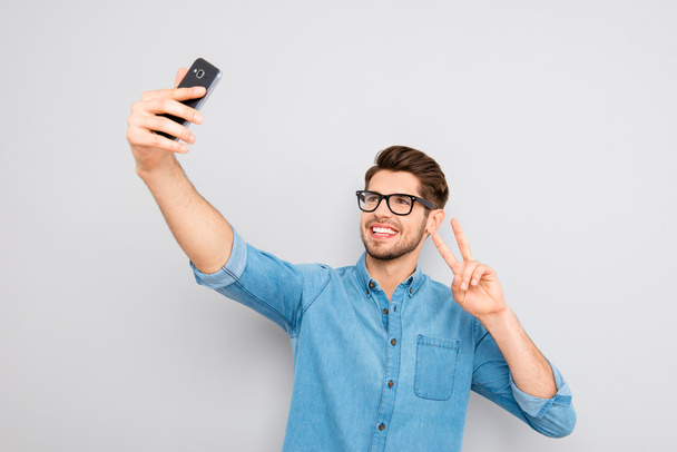 Happy man in glasses making selfie on smartphone and showing two - Photo, Image