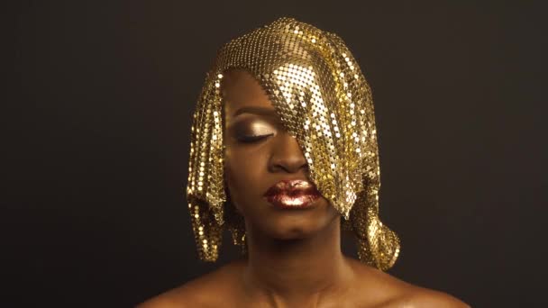 Волшебная сюрреалистичная золотистая африканская модель с ярким блестящим макияжем и блестящей золотистой прической
 - Кадры, видео