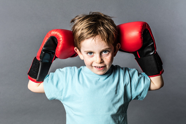 mischievous young boy with freckles holding his boxing gloves up - Fotó, kép