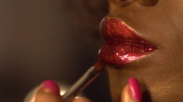 メイクアッププロセスのクローズアップ。アフリカ系アメリカ人女性モデルの大きな赤いセクシーな唇。スタイリストは、ファッション撮影のためのモデルを準備します。ヴォーグコンセプト - 映像、動画