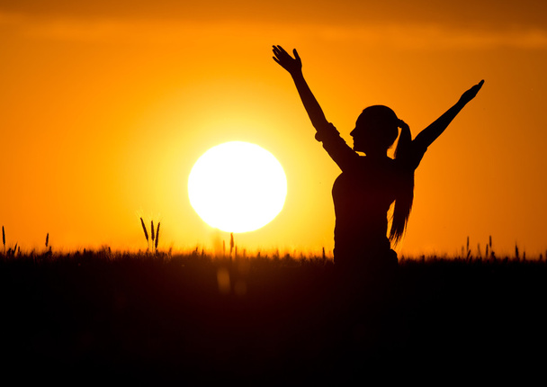 Silhouette of girl with raised hands at sunset - 写真・画像