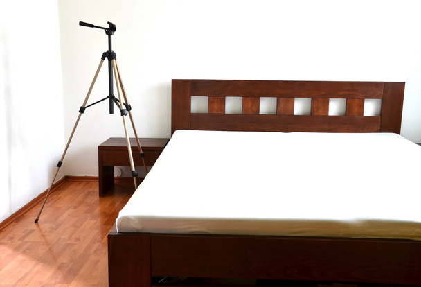Statyw do kamery obok drewniane łóżka w sypialni - Zdjęcie, obraz