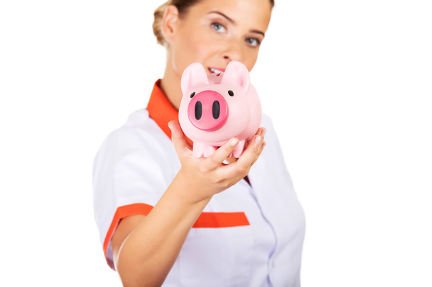 Young beautiful female doctor or nurse holding a piggybank - Zdjęcie, obraz