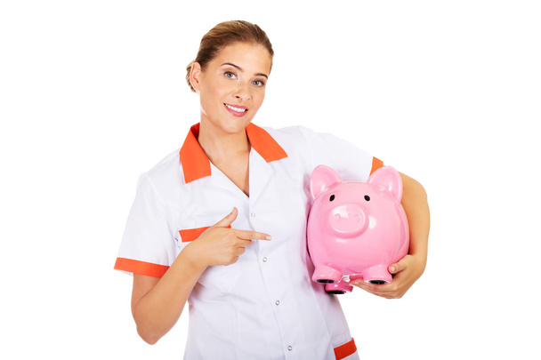 Young beautiful female doctor or nurse holding a piggybank - Photo, Image