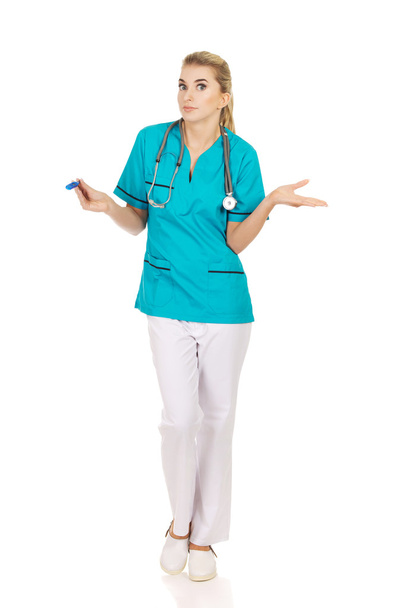 Suprised vrouwelijke verpleegkundige of arts op zoek naar thermometer - Foto, afbeelding