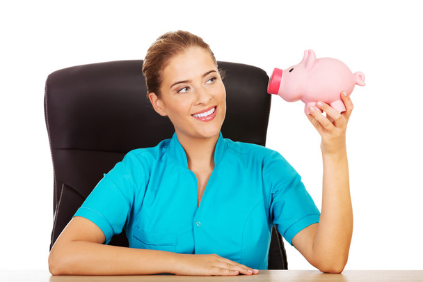 Young female doctor or nurse holding piggybank - Foto, afbeelding