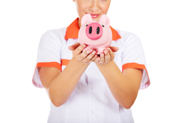 Young beautiful female doctor or nurse holding a piggybank - Zdjęcie, obraz