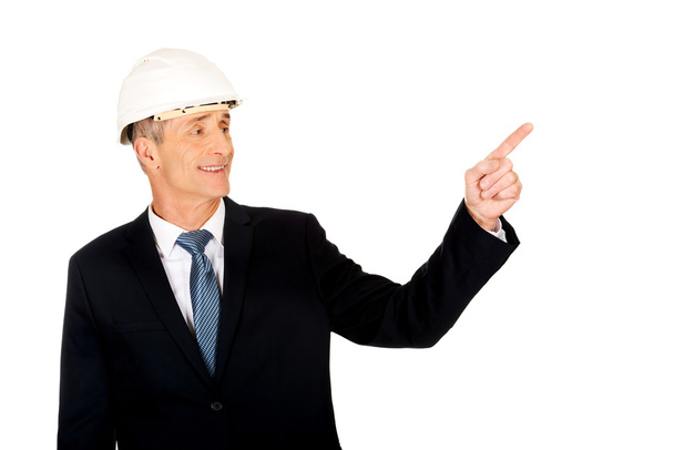 Smiling businessman with hard hat pointing up - Foto, immagini