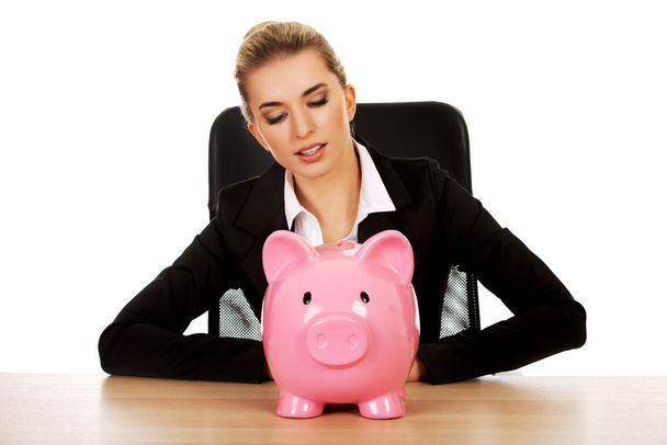 Businesswoman with a piggybank behind the desk - Foto, imagen