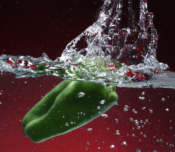 Зеленый перец падает в воду. Красный фон
 - Фото, изображение