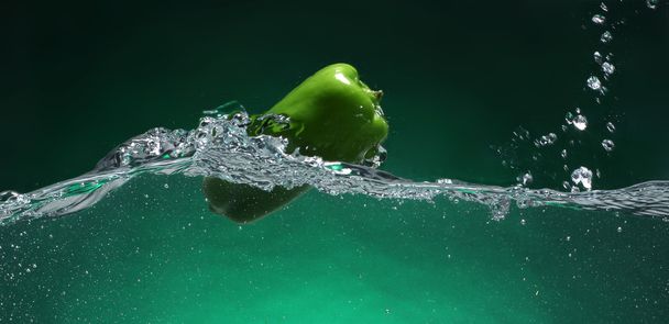 Green pepper falling into water. Green background - Photo, Image