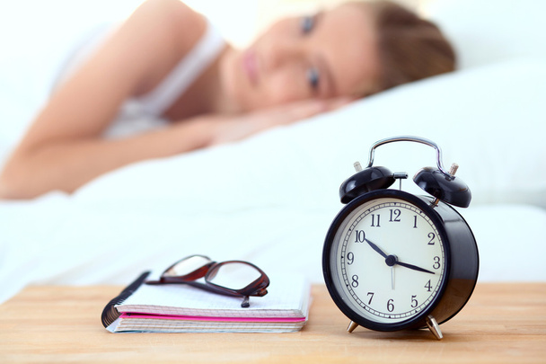 Young sleeping woman and alarm clock in bedroom at home - Foto, Bild