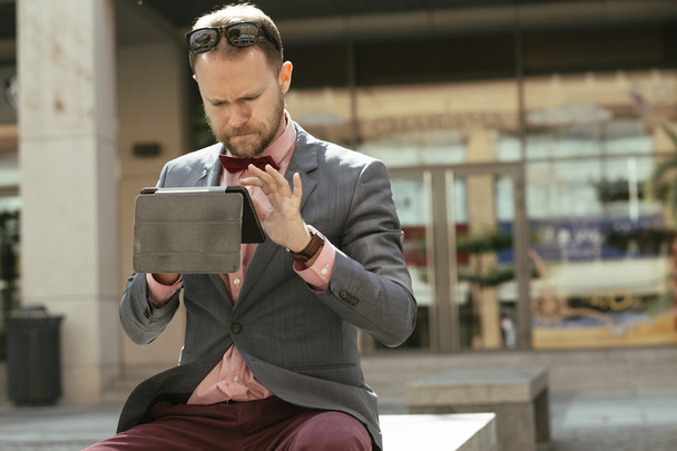 Бизнесмен с помощью цифрового планшета сидит на проспекте города
 - Фото, изображение