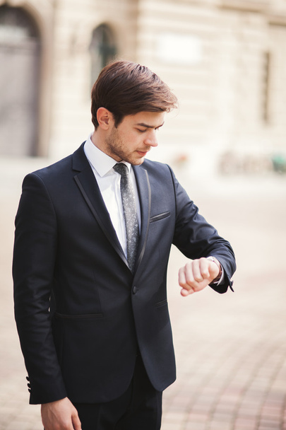 Confident businessman looking on his wrist watch in suit - Zdjęcie, obraz