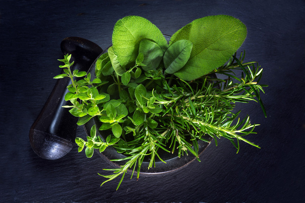 fresh herbs in a mortar with pestle made of black granite on a dark background, view from above - Photo, image
