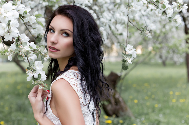 Piękna sexy dziewczyna o długich ciemnych włosach na sukienkę białe latem przechadzającego się po ogrodzie w kwitnących zdjęcie drzewa jabłko w łagodnych tonów - Zdjęcie, obraz
