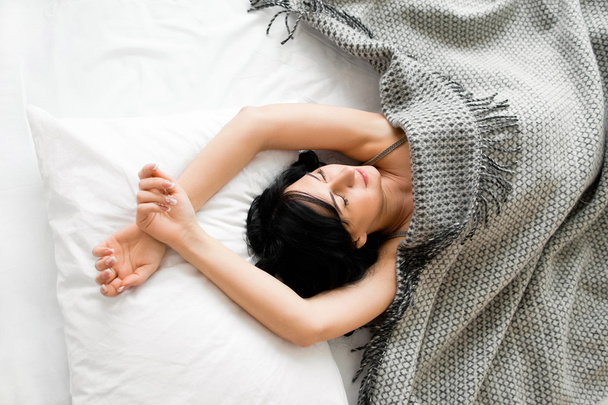 Brunette girl sleep under gray blanket top view - Fotó, kép