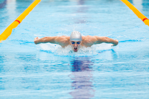 dynamic and fit swimmer in cap breathing performing the butterfly stroke - Zdjęcie, obraz