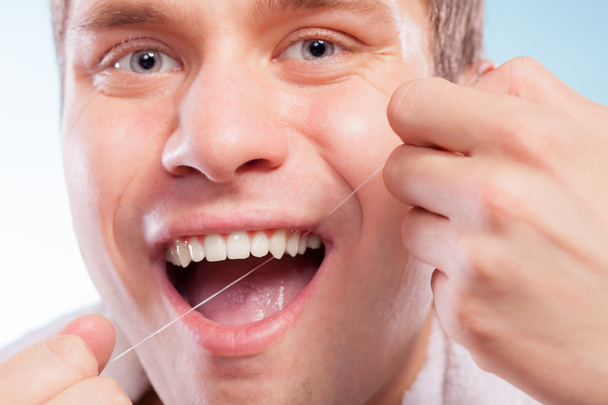 Jonge man haar witte tanden met tandzijde schoonmaken - Foto, afbeelding
