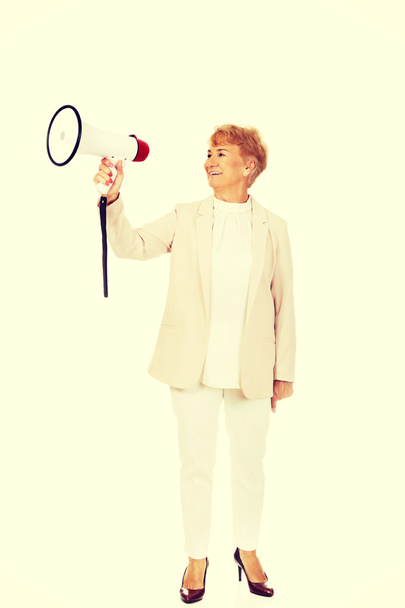 Senior smiling woman screaming through a megaphone - Photo, image