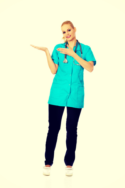 Smiling female doctor or nurse presenting copyspace or something on open palm and pointing for this - Foto, Imagem