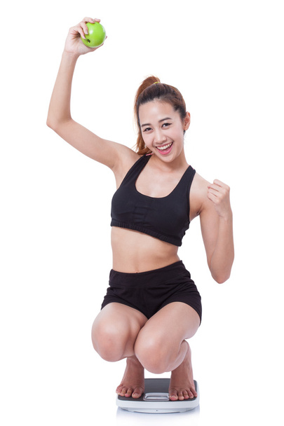 Women on scale cheering for achieving her weight loss goal and green apple. - Photo, Image