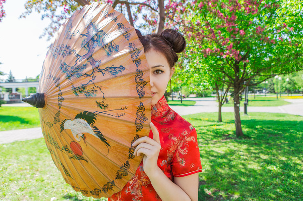 Piękna dziewczyna azjatyckich w tradycyjny chiński czerwony strój z bambusa parasol. - Zdjęcie, obraz