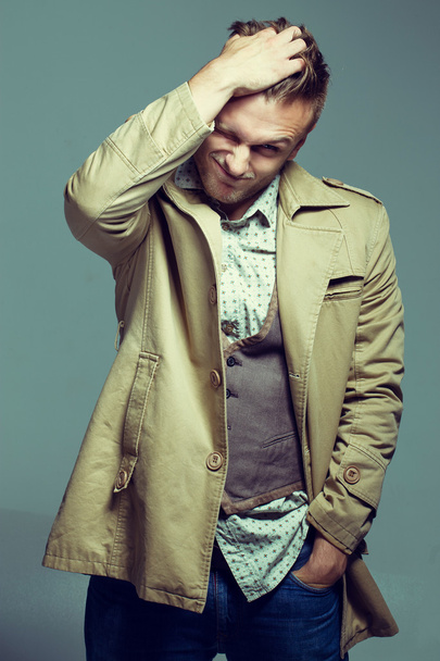 Portret van aantrekkelijke man in trendy mode kleding en jas, poseren in beweging op de grijze achtergrond. Studio opname. Zeer sterke en stijlvolle man - Foto, afbeelding