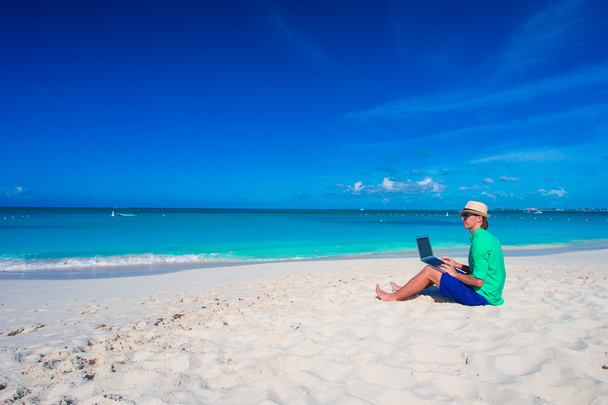 Νεαρός άνδρας με δισκίο υπολογιστή και κινητό τηλέφωνο σε τροπική παραλία - Φωτογραφία, εικόνα