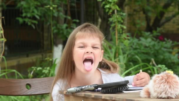Дівчина сидить за столом у дворі і похмуро показуючи язик до рами
 - Кадри, відео