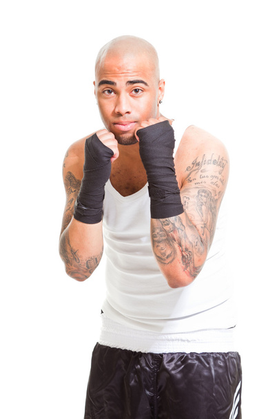 Young male boxer isolated on white background. Wearing white shirt and black shorts. Training outfit. Wet skin from sweating. Tattoos on his arms. - Foto, Imagen
