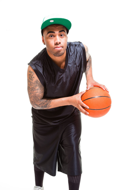 Studio portrait of basketball player wearing green cap standing and holding ball isolated on white. Tattoos on his arms. - Fotó, kép