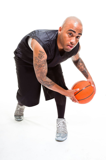 Studioporträt eines Basketballspielers, der isoliert auf weiß steht und Ball hält. Tätowierungen auf seinen Armen. - Foto, Bild